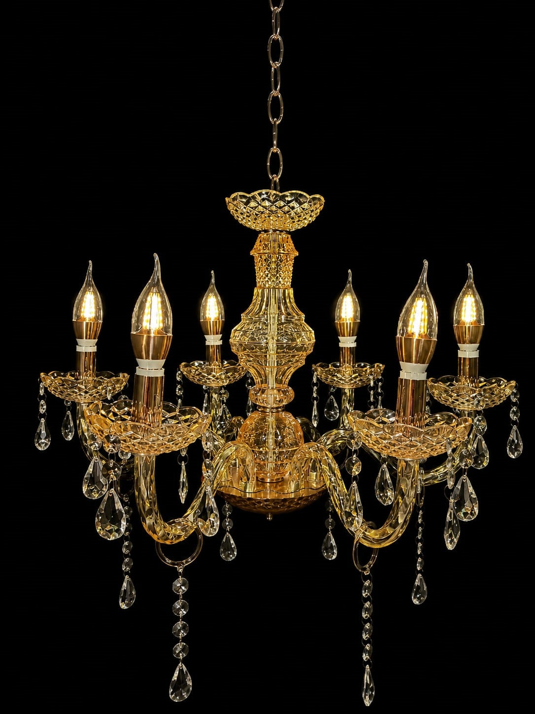 An ornate gold chandelier with six candle-style bulbs, clear crystal teardrop pendants, and a hanging chain